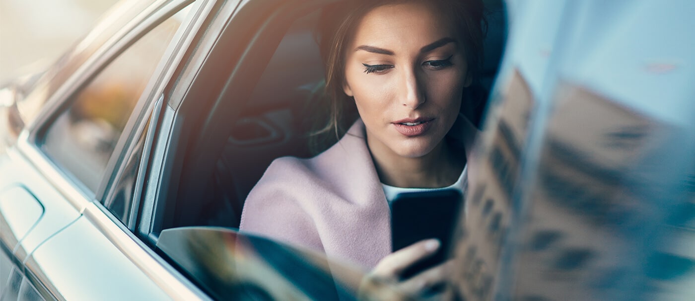 Woman sitting in the back of a car, looking at her phone
