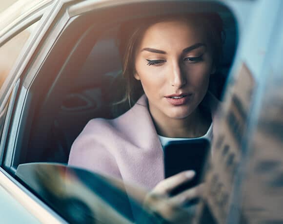 Woman sitting in the back of a car, looking at her phone
