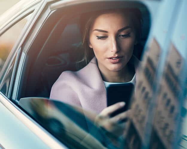 Woman sitting in the back of a car, looking at her phone